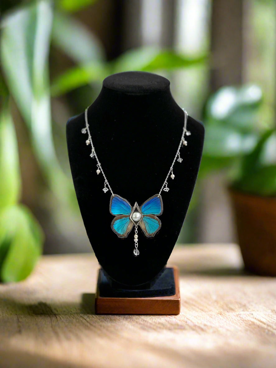 Butterfly-shaped necklace on a black stand with a blurred green background